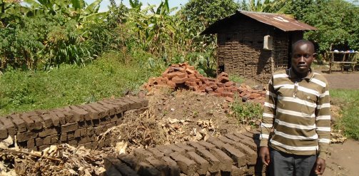 A youth savings group member stands by a stack of bricks he is hoping to sell, Bwera, Kasese District, Uganda