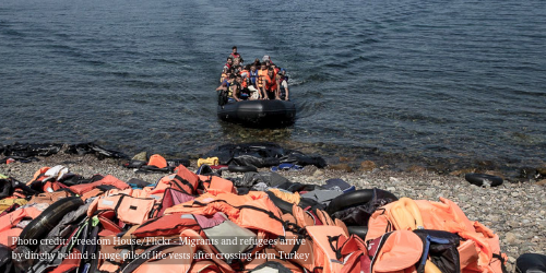 Migrants and refugees arrive by dinghy behind a huge pile of life vests after crossing from Turkey to the island of Lesbos Greece, Sept. 10, 2015.