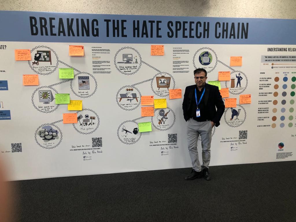 Photograph of a man standing in front of a large visual display called Breaking the Hate Speech Chain