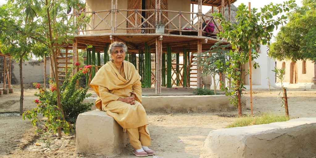 Yesmeen Lari sits on a stone bench in front of a wooden building.