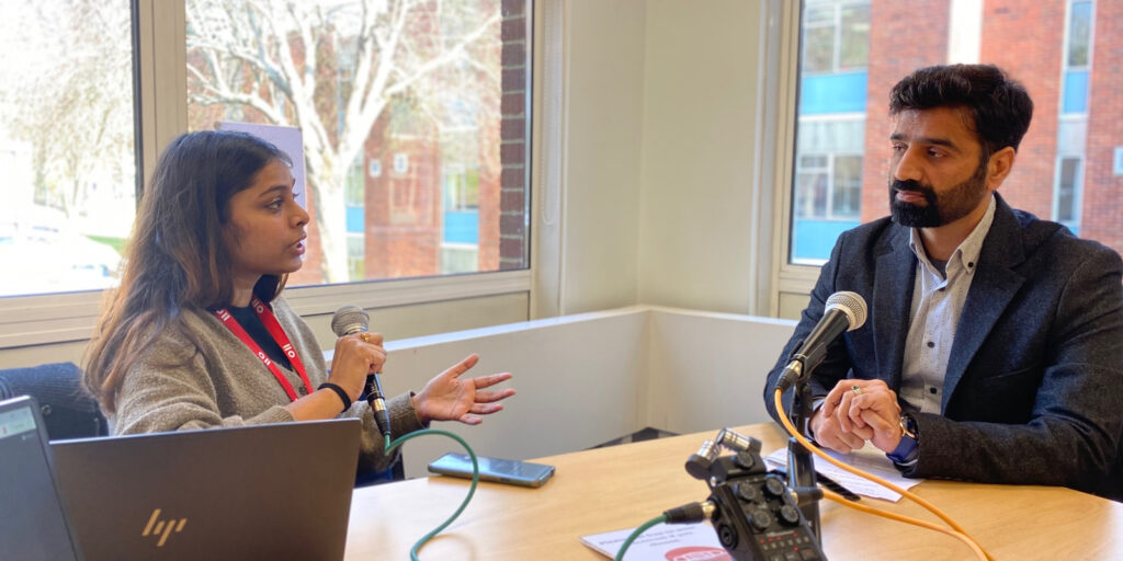 Jigyasa Agarwal (on the left) interviews Naimat Zafary. Both are speaking with microphones as their interview is being recorded on an audio recorder.