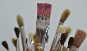 close-up picture of multiple paint brushes. At the center of the frame is a flat brush with bristles pink from usage