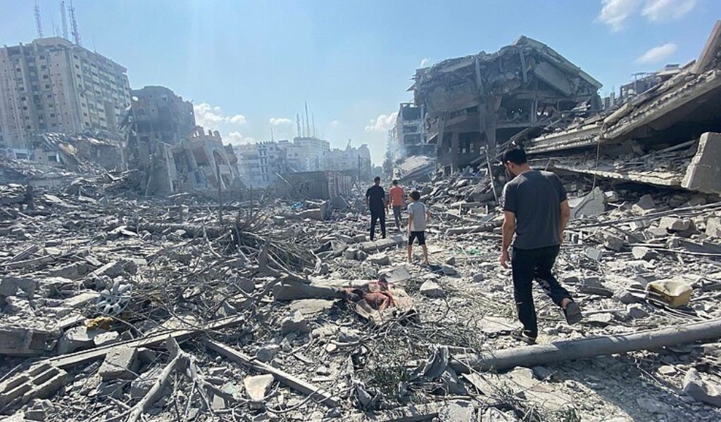 Young men walking away from the camera, over a mass of rubble and the remains of destroyed buildings.