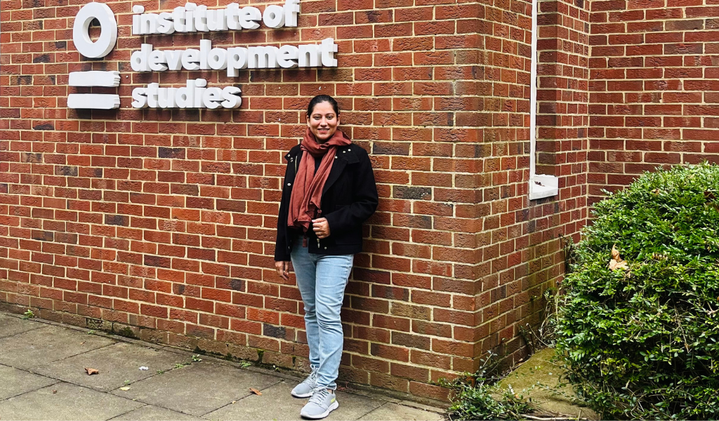 A female student standing in front of a brick wall bearing the IDS logo.