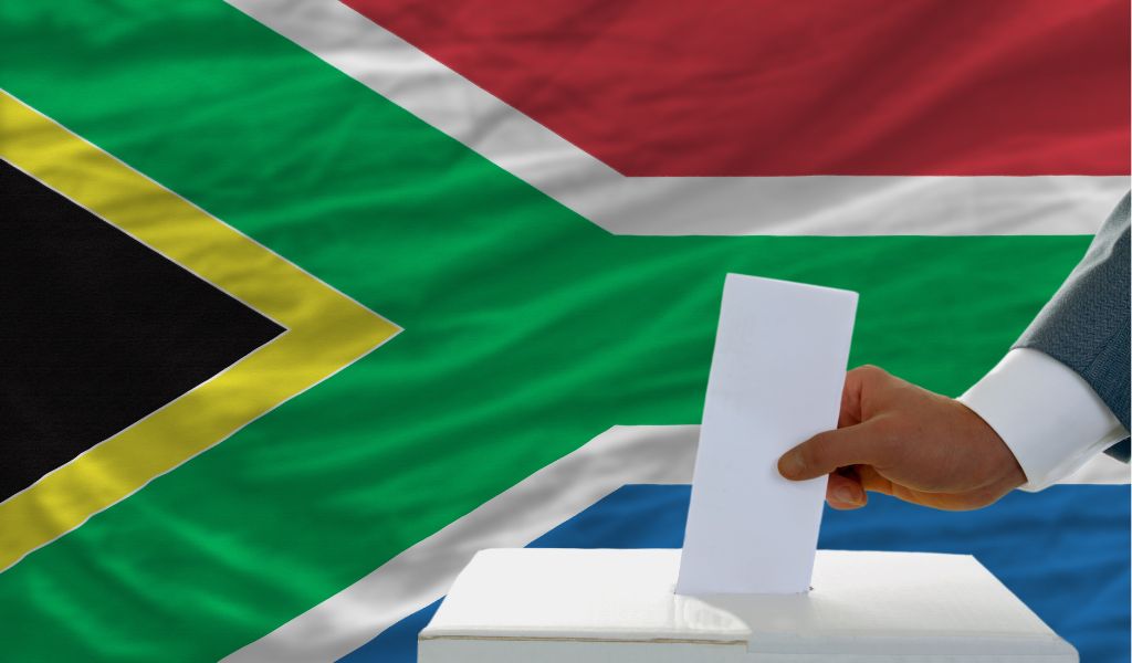 man putting ballot in a box during elections in south africa in front of flag