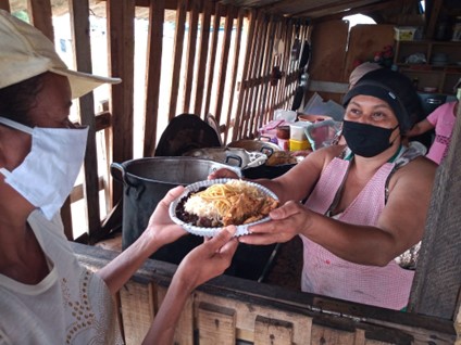 Woman in a face mask giving a plate of food at a solidarity kitchen