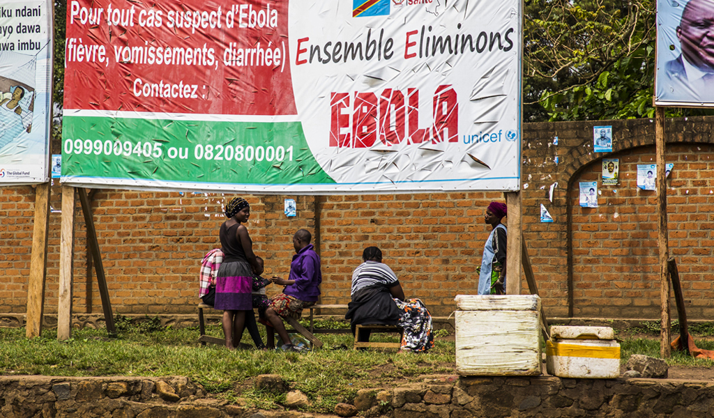 A group of people sit under and large banner which says the words EBOLA.